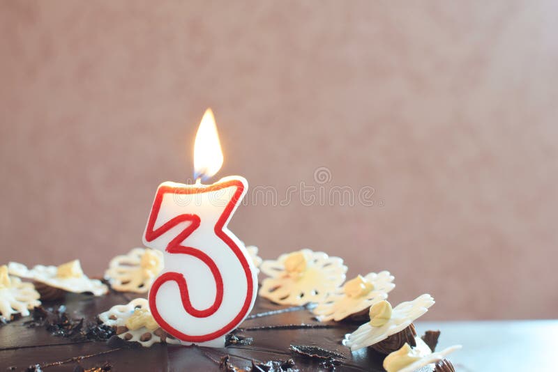 Happy birthday cake for children party decorated with one burning candle in shape of number 3 and sweet candy flowers in honour of third birthday on grunge pink background with copy space for text. Happy birthday cake for children party decorated with one burning candle in shape of number 3 and sweet candy flowers in honour of third birthday on grunge pink background with copy space for text.