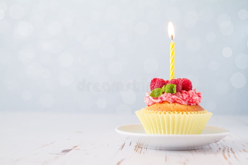 Birthday cupcake with raspberry and candy, light blue bokeh background