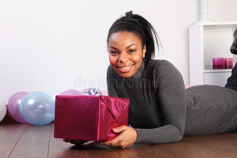 Birthday gift for cheerful african american girl. Happy birthday. Time to celebrate for beautiful young african american girl, lying on the wood floor at home stock image Birthday gift for cheerful african american girl. Happy birthday. Time to celebrate for beautiful young african american girl, lying on the wood floor at home stock image