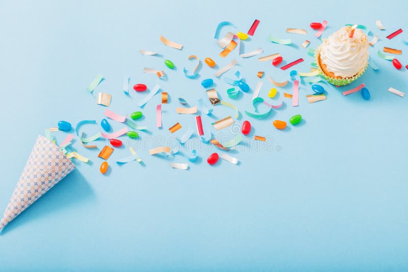 Birthday hat with confetti and cupcake with burning candle on blue paper background. Bright red hat stock images, royalty-free photos and pictures