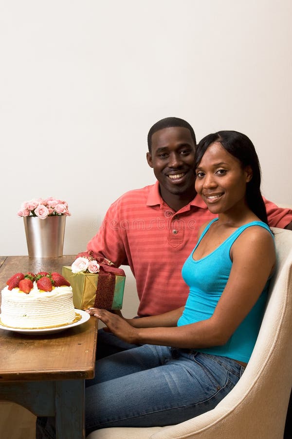 Birthday Party. Attractive smiling couple celebrating a birthday sitting at a table. On top of the table is a frosted cake with strawberries, a wrapped gift, and stock photo Birthday Party. Attractive smiling couple celebrating a birthday sitting at a table. On top of the table is a frosted cake with strawberries, a wrapped gift, and stock photo