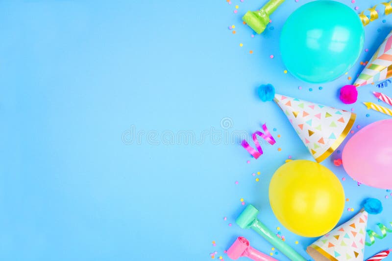 Birthday party side border on a blue background. Above view with confetti, balloons, party hats and streamers. Copy space. Birthday party side border on a blue background. Above view with confetti, balloons, party hats and streamers. Copy space