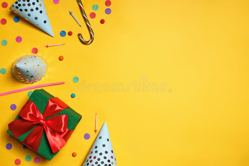 Birthday yellow background with party caps gifts confetti candy copy space.
