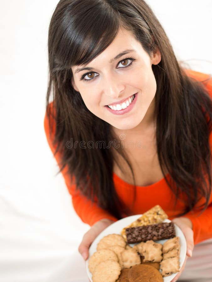 Cute brunette woman eating sweet cereal and chocolate biscuits in bed. Adorable and charming model, looking at camera and smiling. Cute brunette woman eating sweet cereal and chocolate biscuits in bed. Adorable and charming model, looking at camera and smiling.