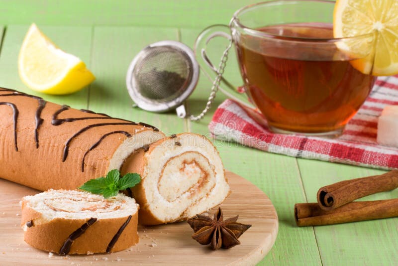 Biscuit Swiss Roll with a Cup of Tea on Green Wooden Background Stock
