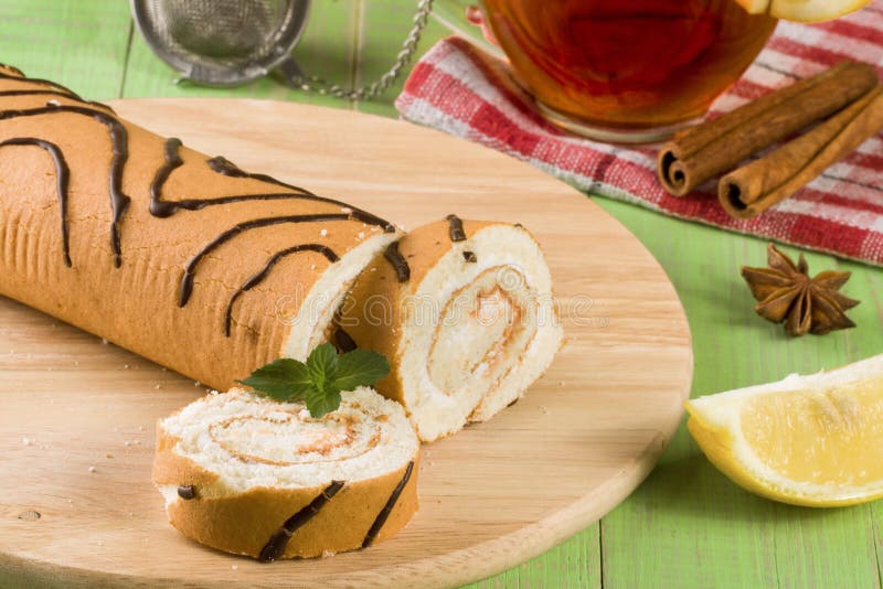 Biscuit Swiss Roll with a Cup of Tea on Green Wooden Background Stock