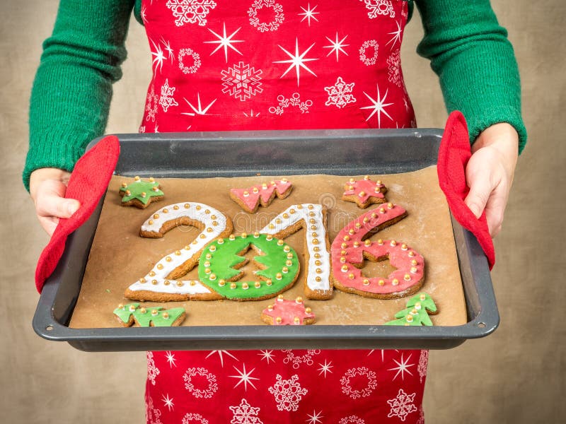 Woman wearing red apron holding home-made gingerbread cookies in shape of 2016 New Year digits on baking tray. Woman wearing red apron holding home-made gingerbread cookies in shape of 2016 New Year digits on baking tray