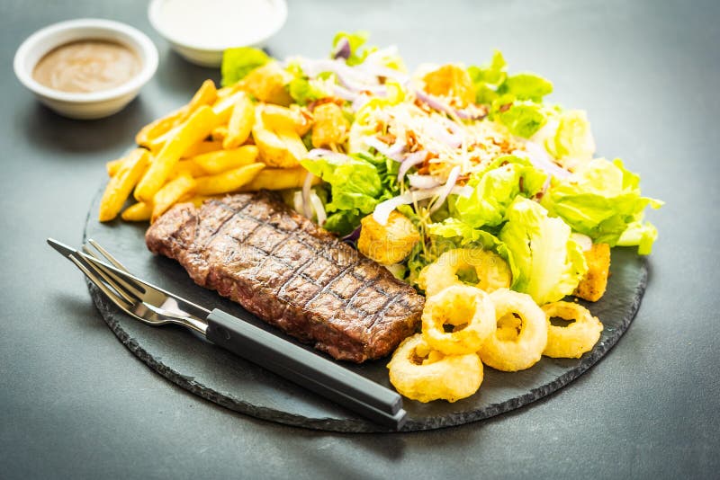 Bistecca arrostita della carne del manzo con l'anello di cipolla delle patate fritte con salsa e la verdura fresca fotografia stock libera da diritti Bistecca arrostita della carne del manzo con l'anello di cipolla delle patate fritte con salsa e la verdura fresca fotografia stock libera da diritti