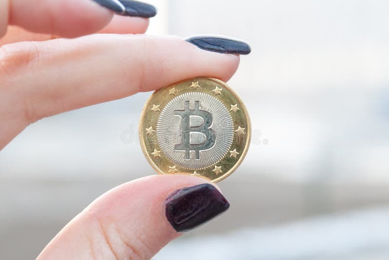Bitcoin dorato della moneta fra il pollice ed i dito indice di una mano femminile con le unghie scure Priorit? bassa vaga Vista d fotografia stock Bitcoin dorato della moneta fra il pollice ed i dito indice di una mano femminile con le unghie scure Priorit? bassa vaga Vista d fotografia stock