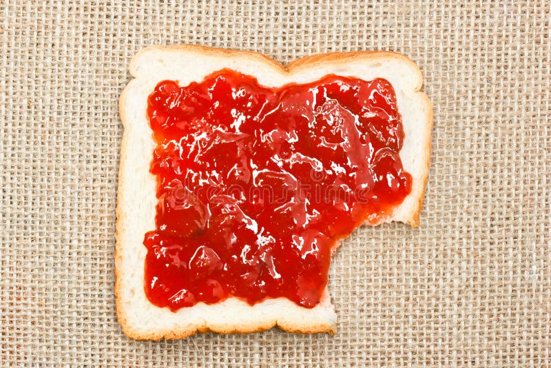 Bite out of a slice of bread with strawberry jam on sacking stock photography