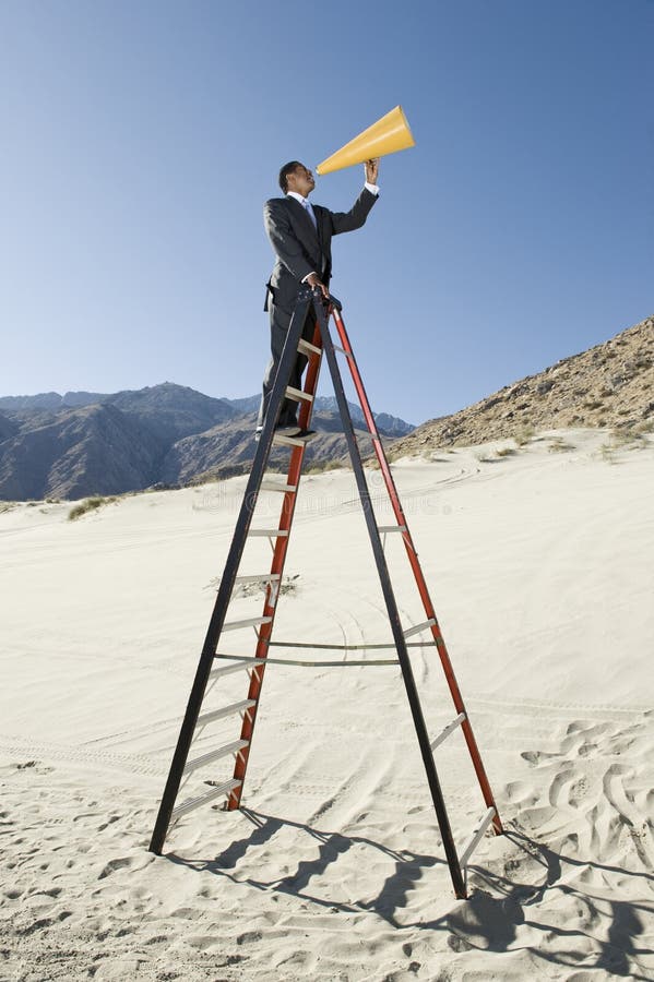 Side view of a businessman standing on stepladder using megaphone in desert. Side view of a businessman standing on stepladder using megaphone in desert