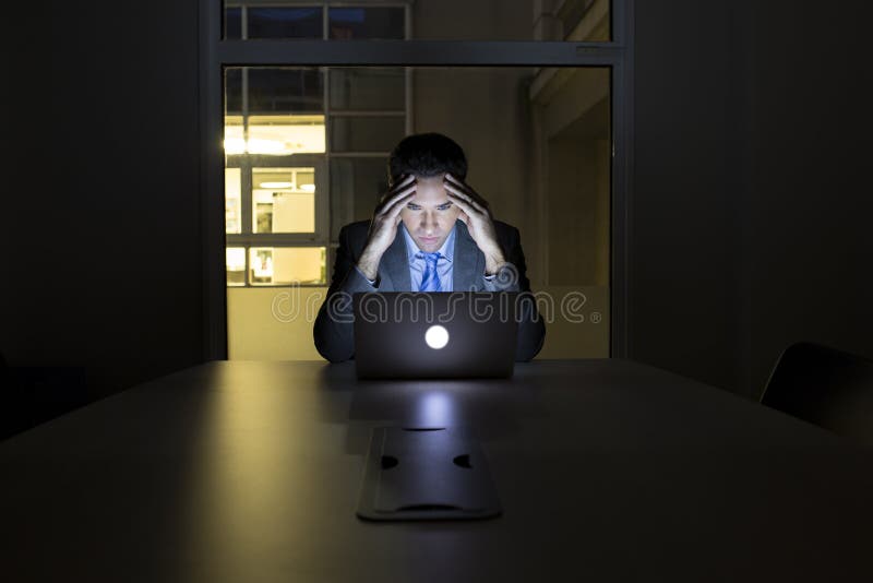 Biznesmen pracuje póżno w jego biurze na laptopie, nocy lekki bu