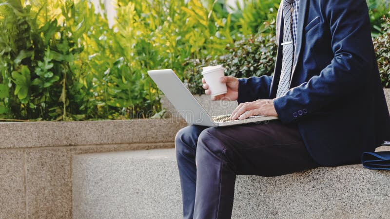 Biznesmen siedzi i pracujący na laptopie o dane zasoby plenerowym z kawą obraz stock Biznesmen siedzi i pracujący na laptopie o dane zasoby plenerowym z kawą obraz stock