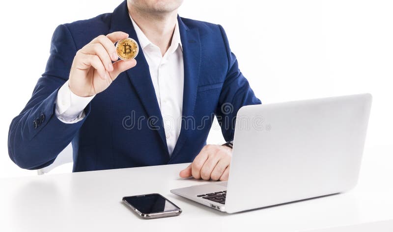 Biznesmen trzyma złotego bitcoin podczas gdy pracujący z laptopem i telefonem przy stołem nad białym tłem zdjęcia stock Biznesmen trzyma złotego bitcoin podczas gdy pracujący z laptopem i telefonem przy stołem nad białym tłem zdjęcia stock