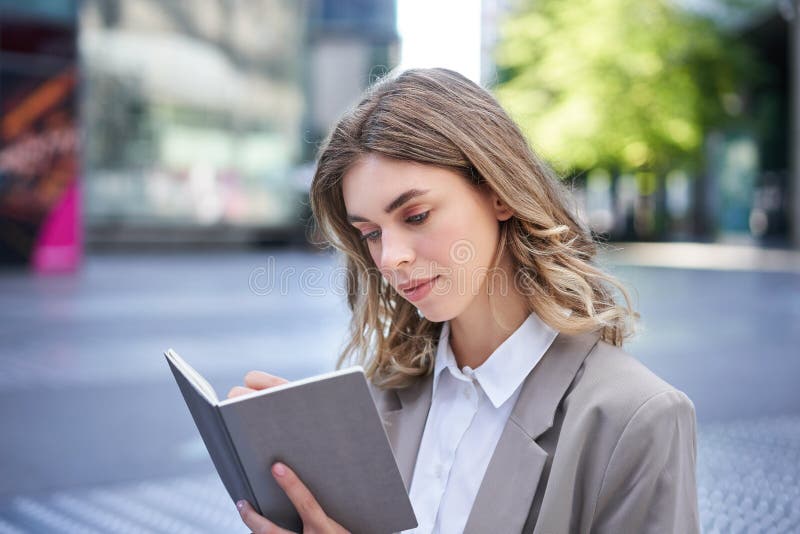 Businesswoman in corporate suit, writes down smth, works on ideas in notebook, sits outside in city centre. Businesswoman in corporate suit, writes down smth, works on ideas in notebook, sits outside in city centre.