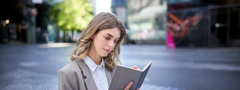 Businesswoman in corporate suit, writes down smth, works on ideas in notebook, sits outside in city centre. Businesswoman in corporate suit, writes down smth, works on ideas in notebook, sits outside in city centre.