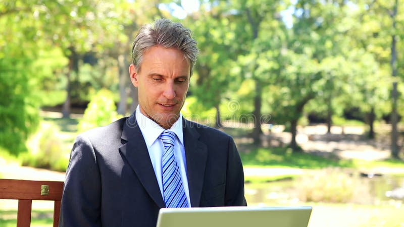 Biznesmena obsiadanie na parkowej ławce używać jego laptop