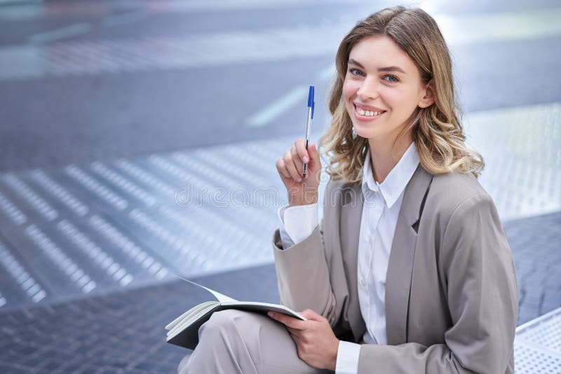 Business woman in suit sits in city centre, writes down, takes notes, holds pen and notebook, brainstorms, creates ideas. Business woman in suit sits in city centre, writes down, takes notes, holds pen and notebook, brainstorms, creates ideas.