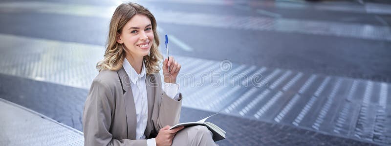 Business woman in suit sits in city centre, writes down, takes notes, holds pen and notebook, brainstorms, creates ideas. Business woman in suit sits in city centre, writes down, takes notes, holds pen and notebook, brainstorms, creates ideas.