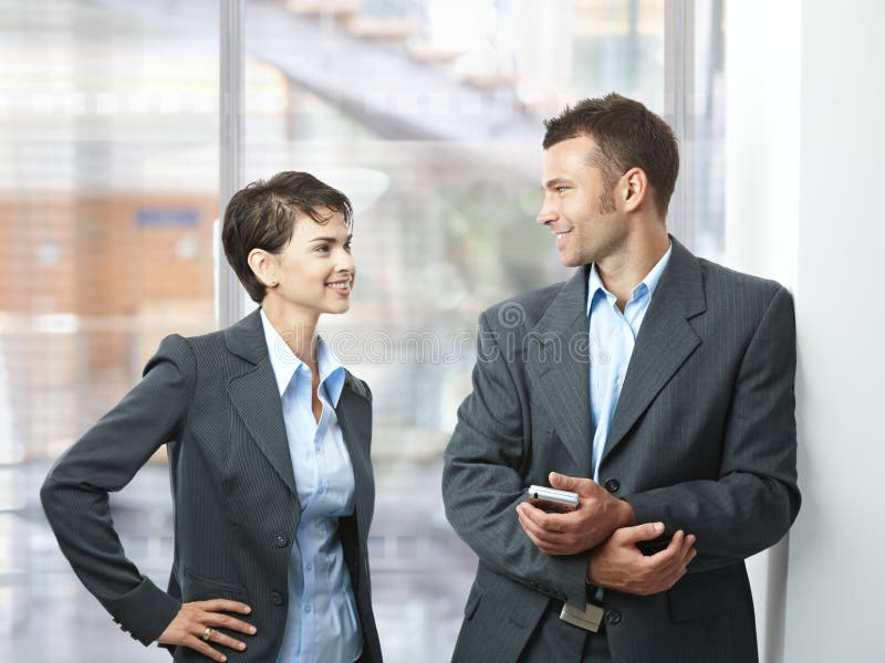 Two happy businesspeople talking in office lobby, looking at each other, smiling. Two happy businesspeople talking in office lobby, looking at each other, smiling.