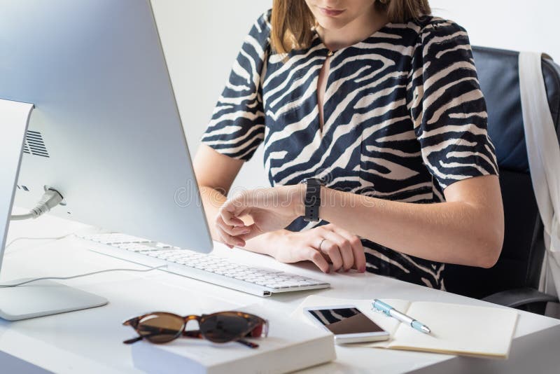 Biznesowa kobieta sprawdza czas przy biurkiem w nowożytnym minimalistic offi zdjęcie stock Biznesowa kobieta sprawdza czas przy biurkiem w nowożytnym minimalistic offi zdjęcie stock
