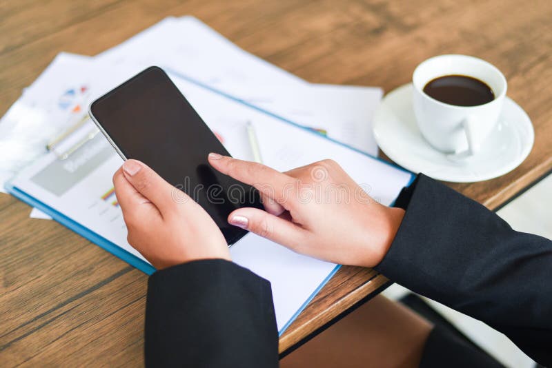 Biznesowa kobieta używa smartphone i działanie w biurze z biznesowym raportem na stołowym biurku z filiżanką - kobiety używają zdjęcia stock Biznesowa kobieta używa smartphone i działanie w biurze z biznesowym raportem na stołowym biurku z filiżanką - kobiety używają zdjęcia stock