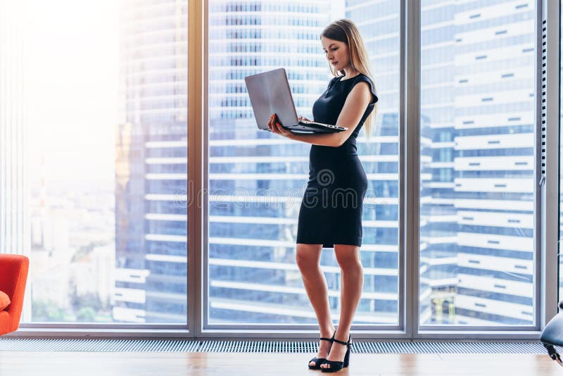 Bizneswomanu mienia laptopu pozycja w nowożytnym biurze przeciw okno z miasto widokiem zdjęcie royalty free Bizneswomanu mienia laptopu pozycja w nowożytnym biurze przeciw okno z miasto widokiem zdjęcie royalty free