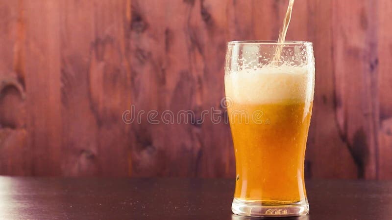 Bière de versement en verre avec la mousse blanche sur le bois