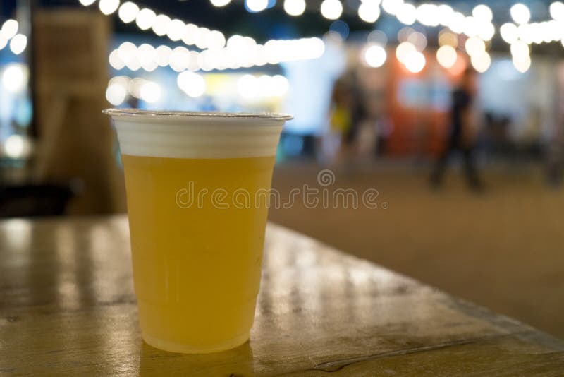 Bière pression dans la tasse en plastique sur la table en bois au festival avec la lumière de bokeh photo libre de droits Bière pression dans la tasse en plastique sur la table en bois au festival avec la lumière de bokeh photo libre de droits
