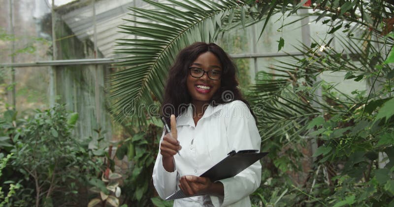 Bióloga o científica afroamericana trabajando en un jardín botánico. guarda un bloc de notas y muestra la conformidad con la cámar almacen de metraje de vídeo