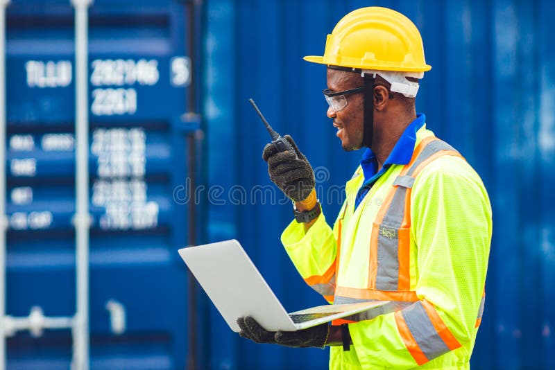 Black African happy worker working in logistic communication using radio and laptop to control loading containers at port cargo to