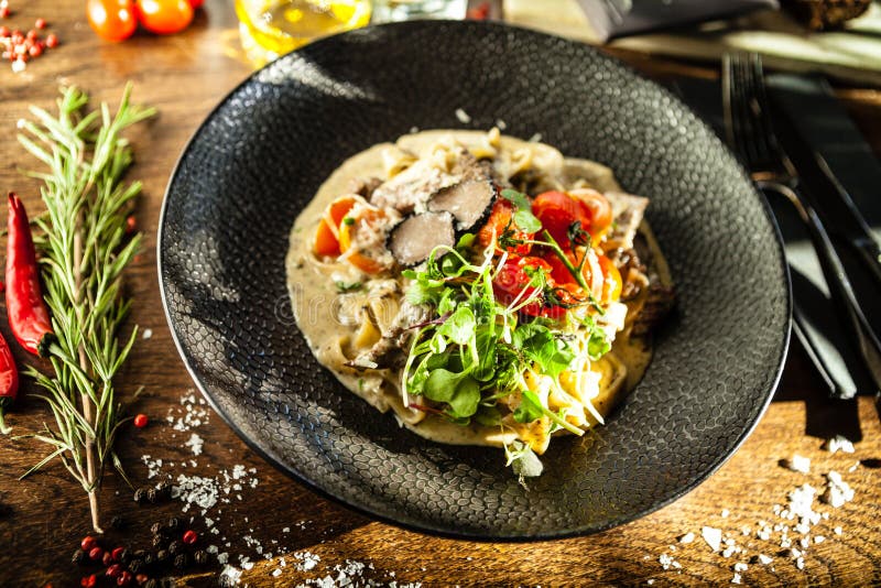 Black Angus beef tagliatelle pasta with fresh black truffles and parmegano. Delicious healthy traditional food closeup served for lunch in modern gourmet cuisine restaurant.