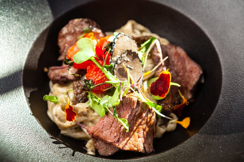 Black Angus beef tagliatelle pasta with fresh black truffles and parmegano. Delicious healthy traditional food closeup served for lunch in modern gourmet cuisine restaurant.