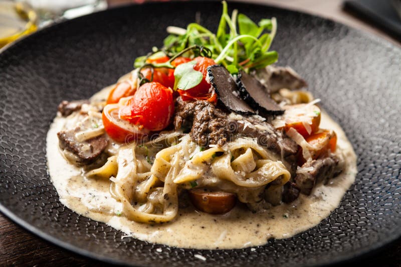 Black Angus beef tagliatelle pasta with fresh black truffles and parmegano. Delicious healthy traditional food closeup served for lunch in modern gourmet cuisine restaurant.