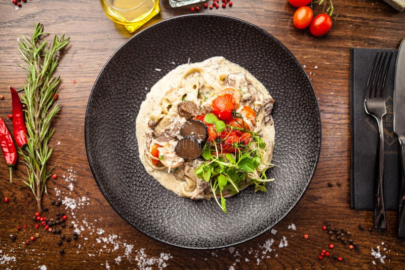 Black Angus beef tagliatelle pasta with fresh black truffles and parmegano. Delicious healthy traditional food closeup served for lunch in modern gourmet cuisine restaurant.