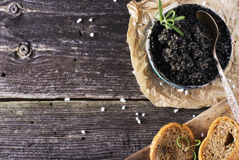 Black Astrakhan Russian salted sturgeon caviar in a can on dark background with wooden spoon and slices of bread. Snacks