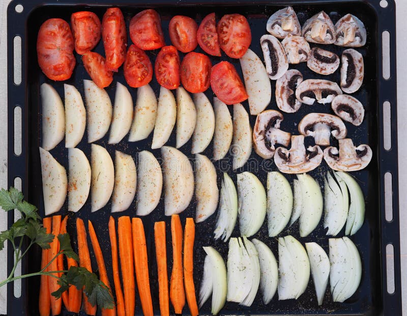 Black baking tray from a home oven with sliced vegetables for baking or drying.Homemade cooking with chips and baked vegetables. stock photos