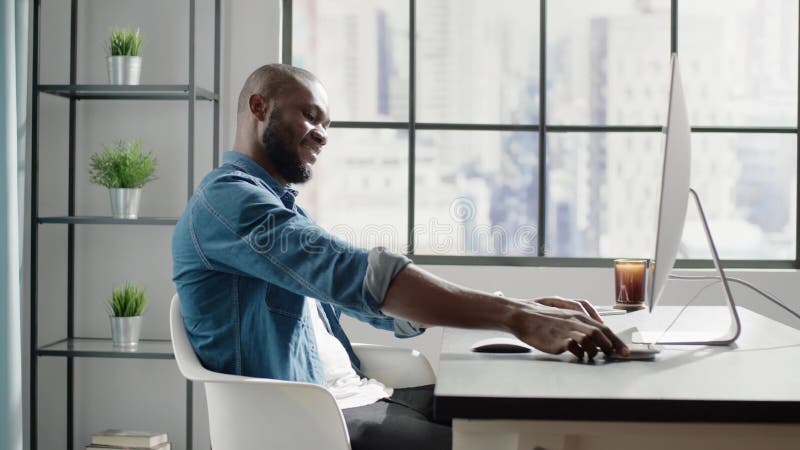 Black bald man chats on smartphone at contemporary computer