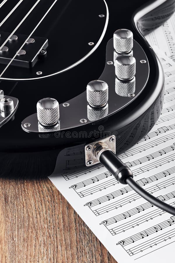 Black bass guitar and knobs with jack cable on sheet music and wooden table stock photography
