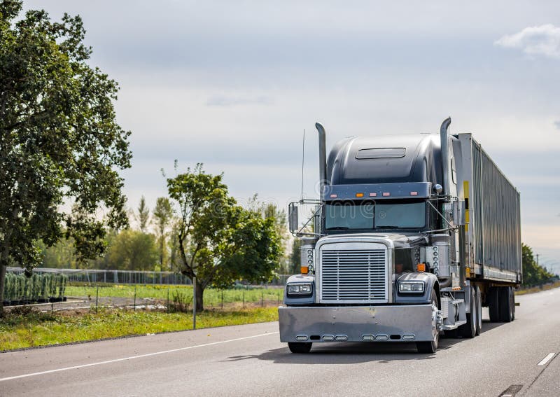 Schwarz klassisch der große ausrüstung Dieselkraftstoff industriell Deckel lange Zeit ziehen halbfertige produkte LKW tragen kommerziell Ladung auf der halbfertige produkte anhänger laufen auf der breit Autobahn Straßen Grün Bäume auf der Seite.