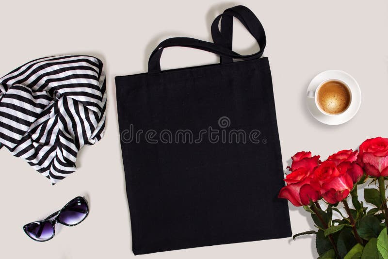 Black blank cotton eco tote bag with red roses, glasses, scarf and a cup of coffee, styled design mockup.