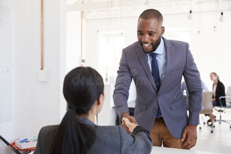 Black businessman and seated woman shaking hands in office royalty free stock photography