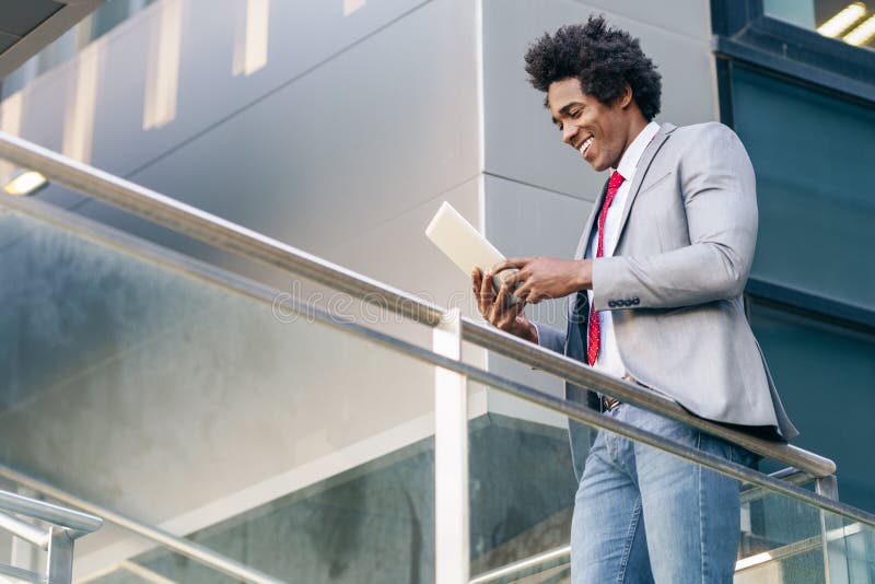 Black Businessman using a digital tablet sitting near an office building.