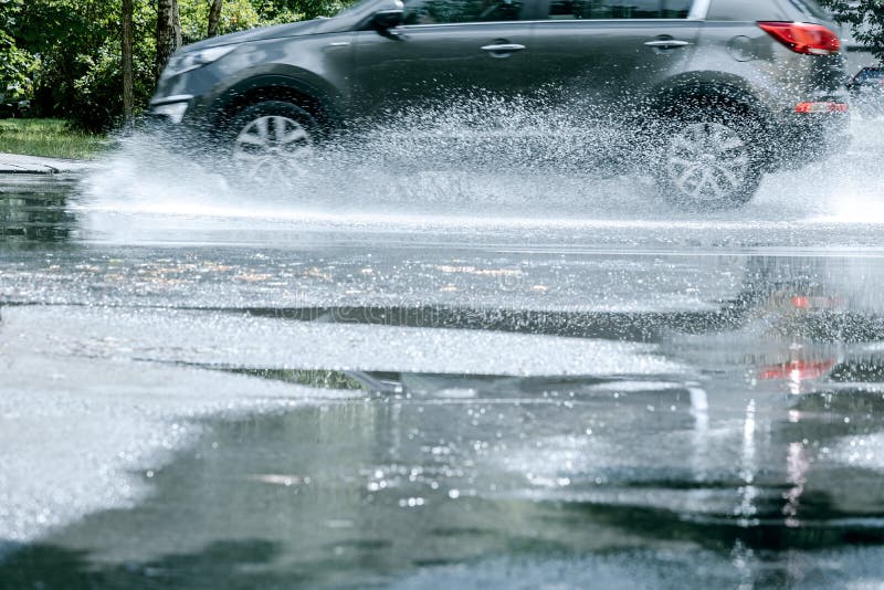 Black Car Driving through Rain Puddle and Reflecting in it Stock Image