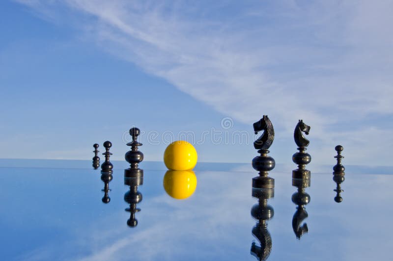 Black chess pieces and yellow billiards ball on mirror