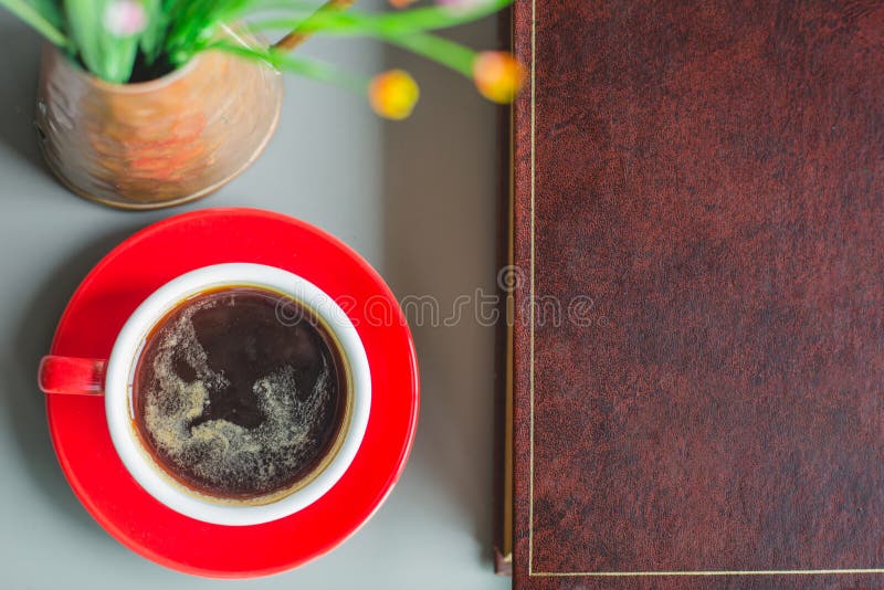 Black Coffee in Red Cup with Book and Clock on Table in Cafe. Stock