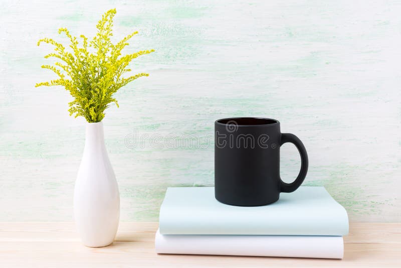 Black coffee mug mockup with ornamental green grass and books.