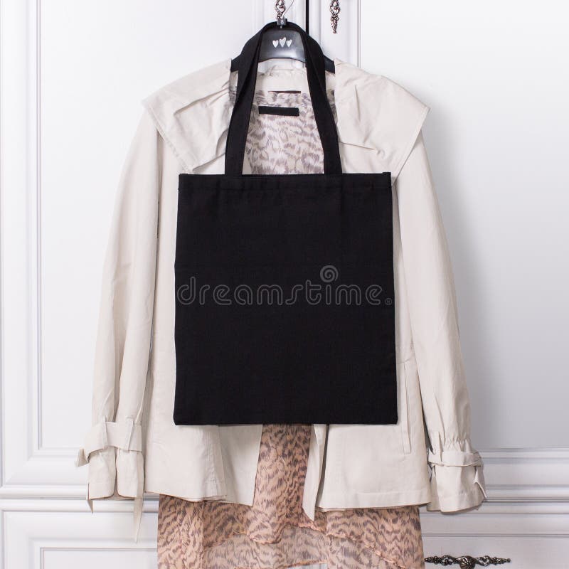 Black cotton eco tote bag on a hanger with elegant clothes, design mockup. Handmade shopping bags. Spring collection.