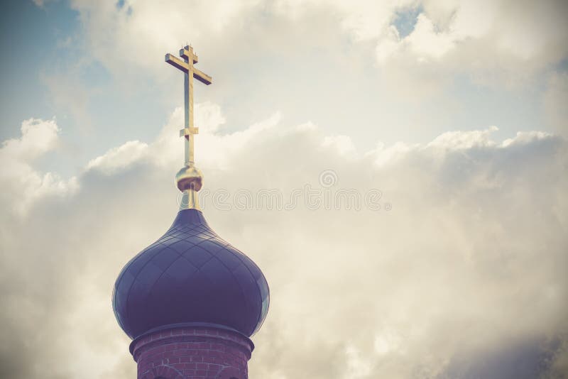 Black dome of the Church with a golden cross on the sky background with white clouds. tower of the old red brick in the light of t