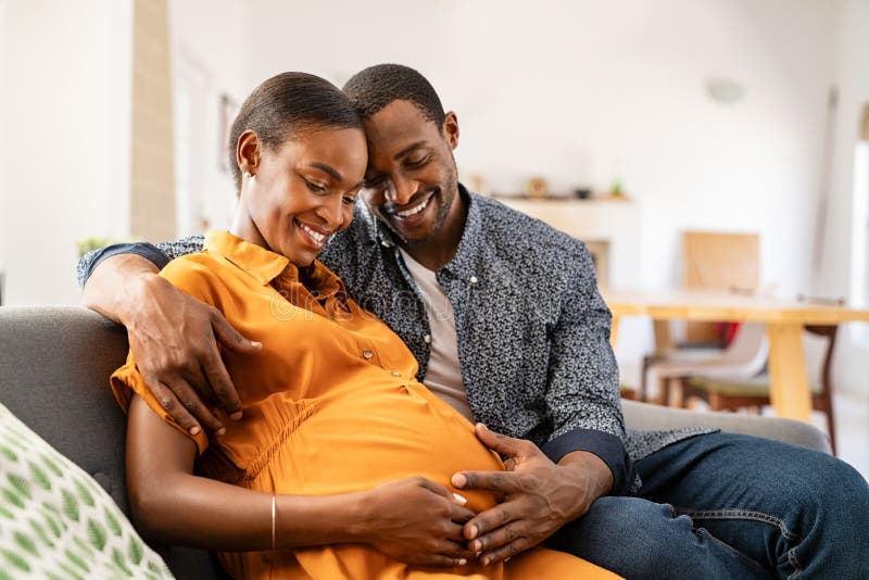 Black Expectant Parents Sitting on Sofa Dreaming about Their Baby Stock